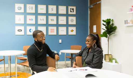 Two students sitting side by side at a study table. Both students are smiling.