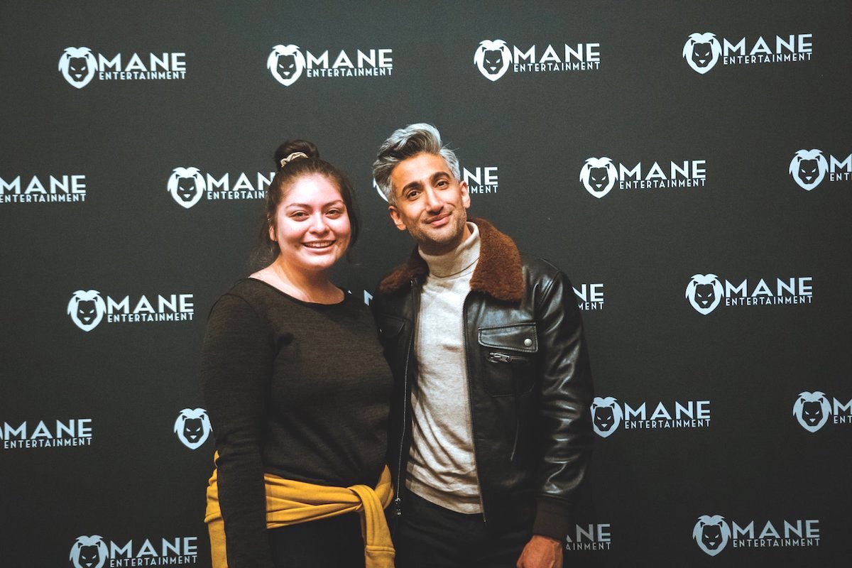 Student posing in front of Mane Entertainment background with Tan France.